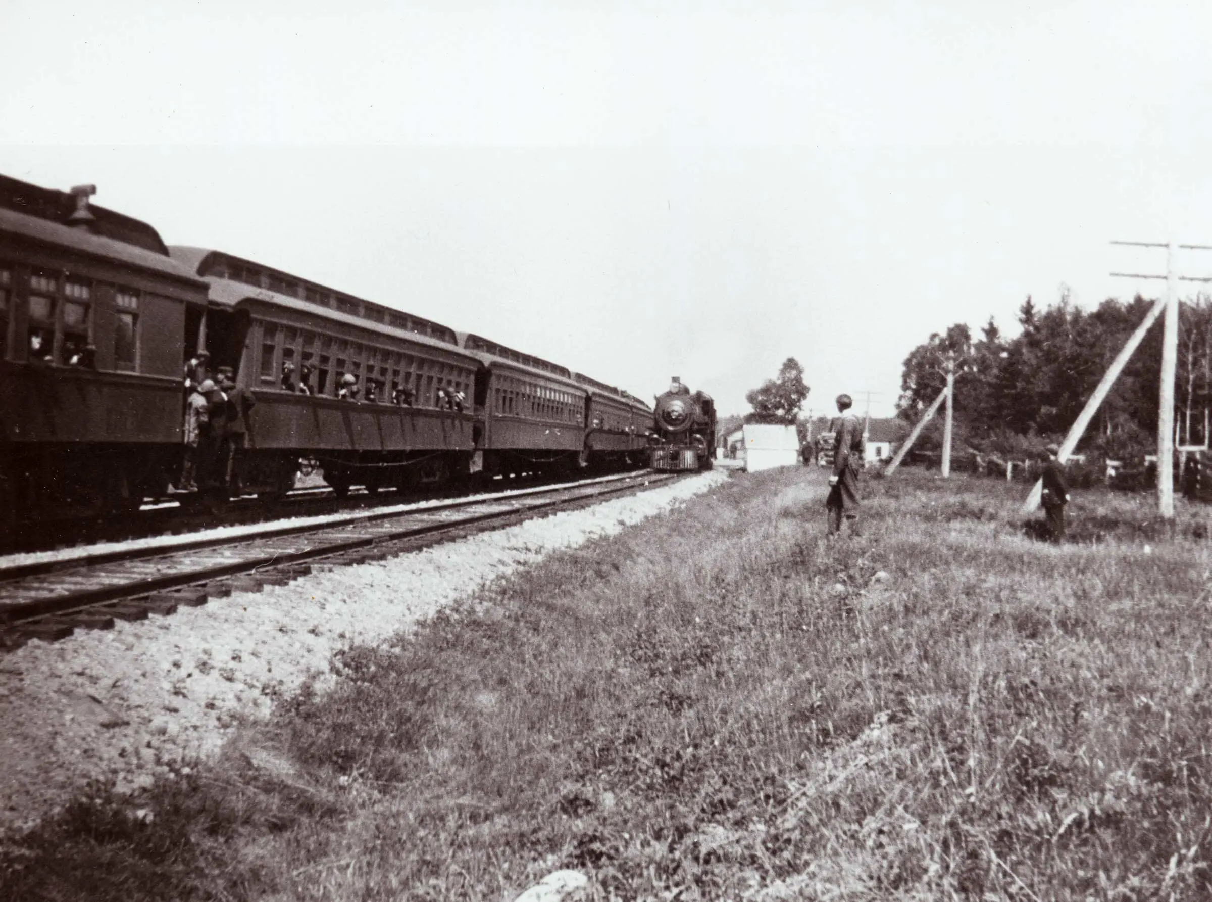A long train on a curving track with some passengers leaning out of the windows.