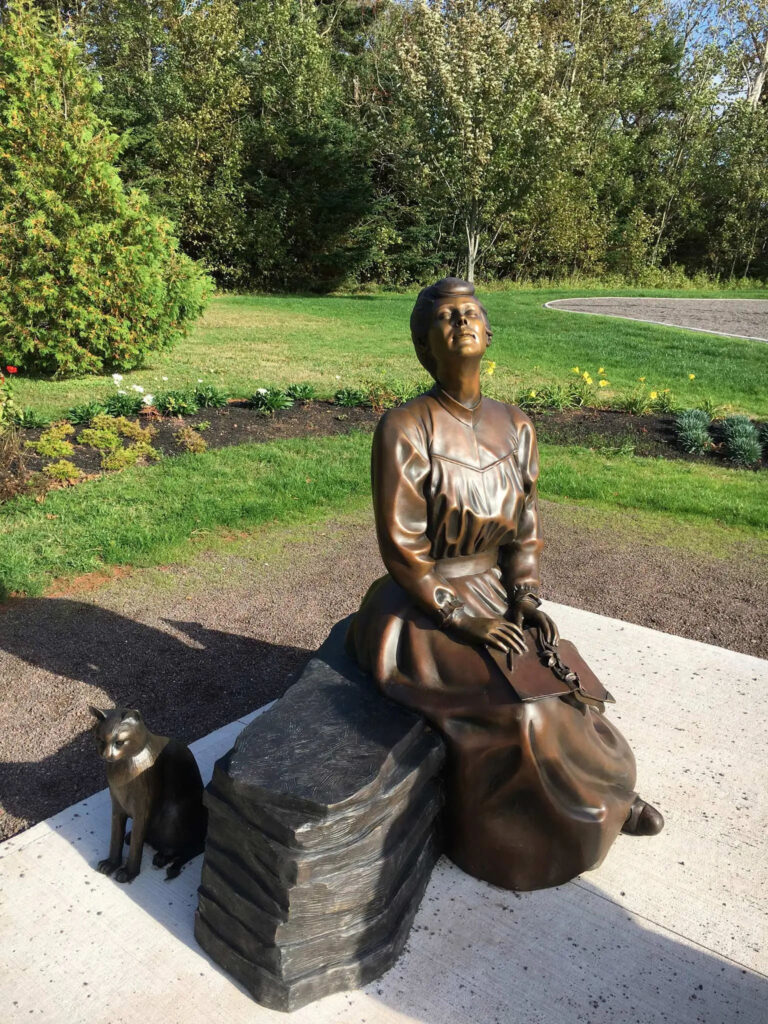 statue en bronze représentant une femme en jupe longue, un livre sur les genoux, le visage levé vers le soleil