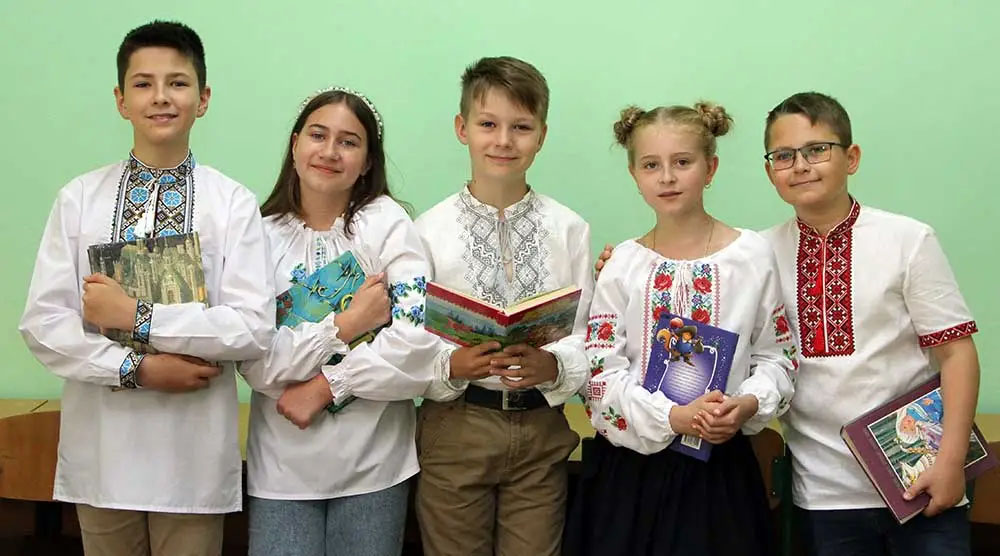cinq jeunes enfants debout en ligne tiennent des livres.