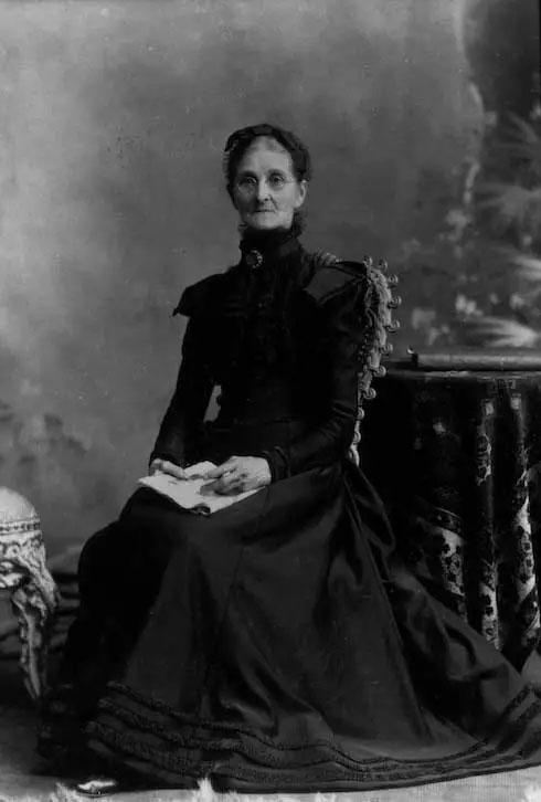black and white photo of an older woman in a black dress, seated and holding a book