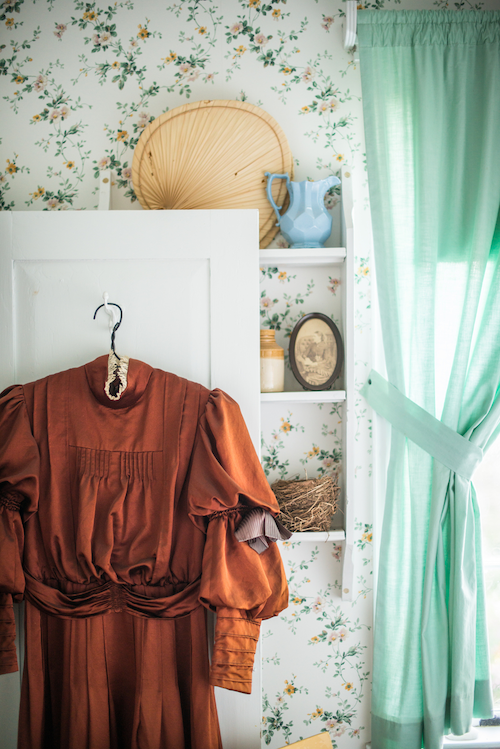 robe brune avec deux bouffants par manche suspendue sur la porte blanche d’un placard dans une chambre ensoleillée