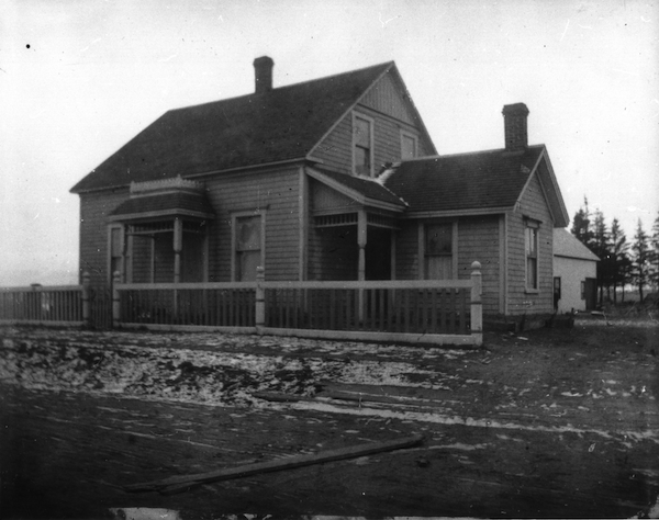 black and white photo of a small house with a covered front step and small chimney sticking up from the middle