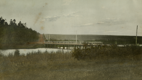 hand-tinted image of a long pond with a wooden bridge across it. the bridge has thick log piles