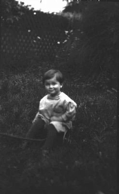 Photographie en noir et blanc d’un petit enfant aux cheveux foncés sur la pelouse.