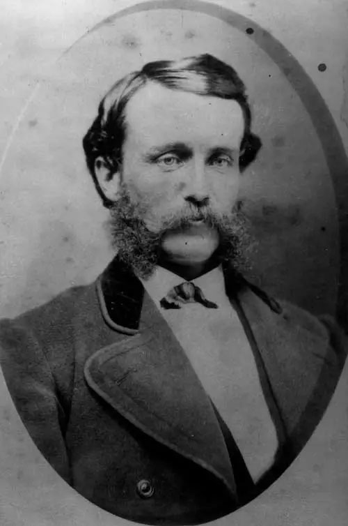Photo d’un jeune homme portant une grande moustache et des favoris, dans un passe-partout ovale.