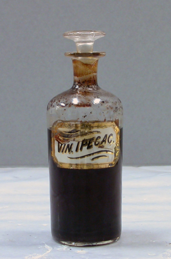 an old fashioned glass bottle with a gilt label, filled partway with a brown liquid