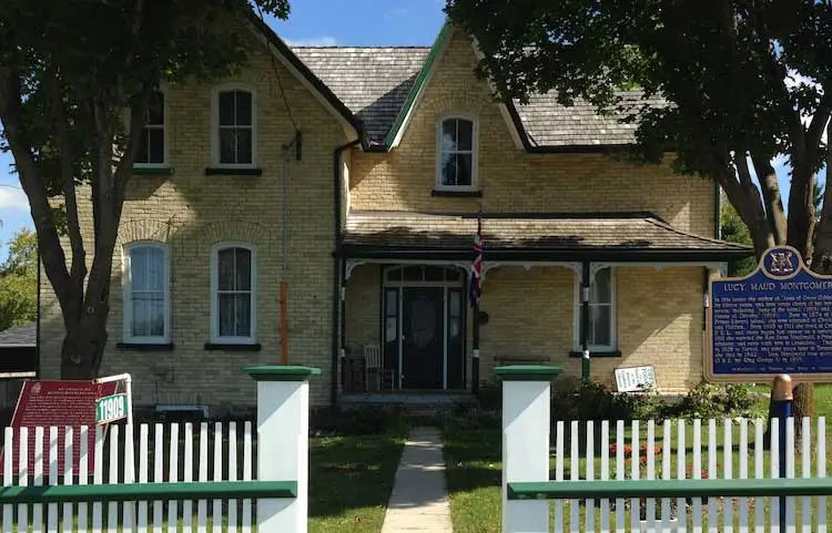 Une maison de briques beiges ornée de lisières vert foncé ayant une porte de la même couleur ainsi qu’une clôture de piquets blancs.