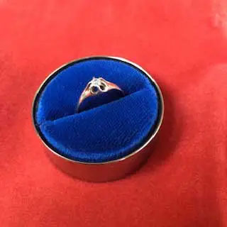 Une bague à diamant solitaire en or ornée de détails filigranes dans un étui en velours bleu sur fond rouge.