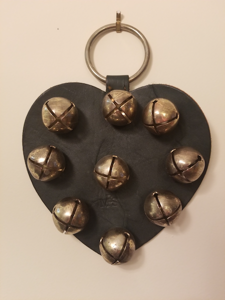 pièce de cuir en forme de cœur à laquelle sont attachées neuf cloches rondes, surmontée d’un anneau de métal