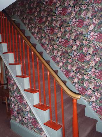 a steep staircase with red railings, surrounded by a busy floral wallpaper