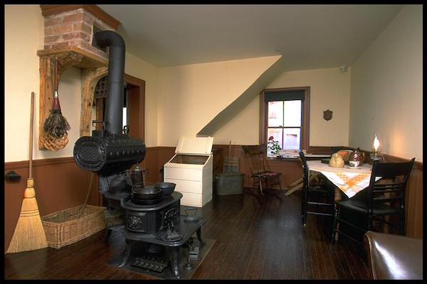a farmhouse kitchen with a large woodbox, table, and a prominent black stove