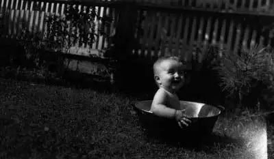 Photographie présentant un bébé joyeux dans une bassine en étain placée sur le gazon.